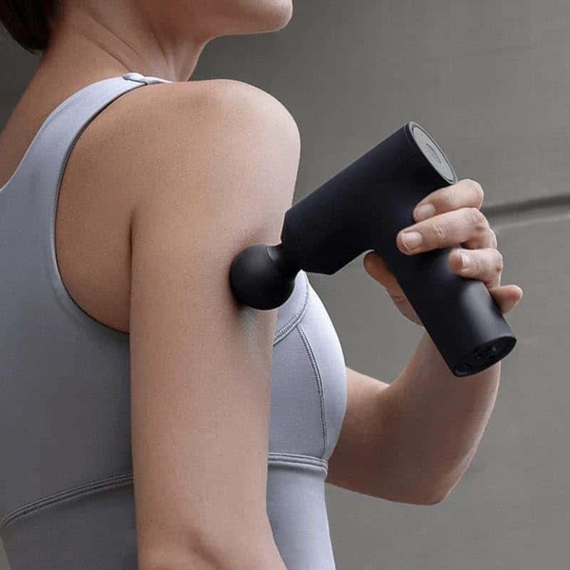 Deportista usando una pistola de masaje Xiaomi en el brazo para aliviar tensión muscular